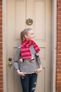 young girl wearing pink and red scarf with pom poms on the ends